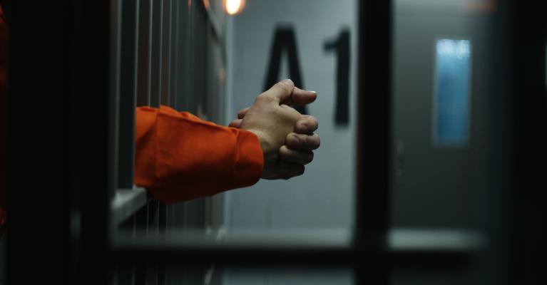 Mann i fengsel stikker hendene ut gjennom gitteret