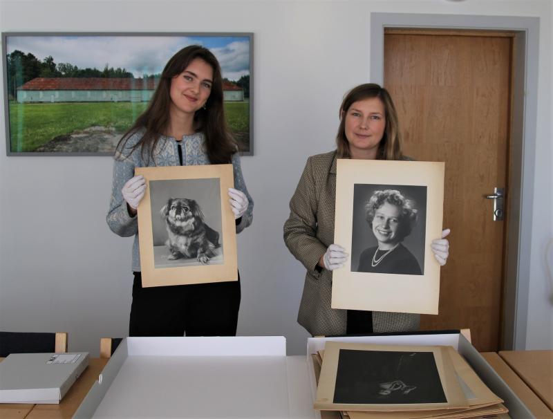 To kvinner viser frem svart-hvitt-foto av en dame og en hund
