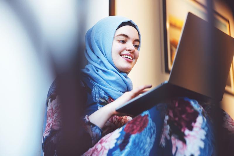 Ung kvinne fra Midtøsten med hijab skriver på pc