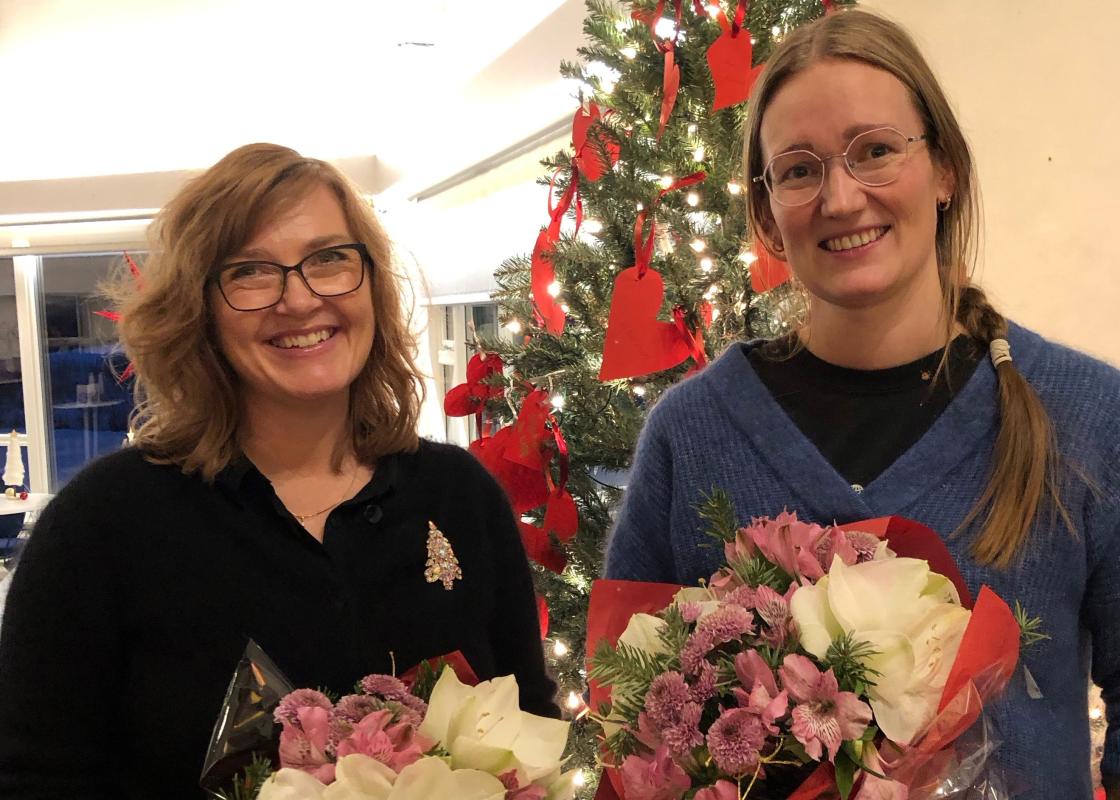To kvinner med blomsterbuketter foran juletre