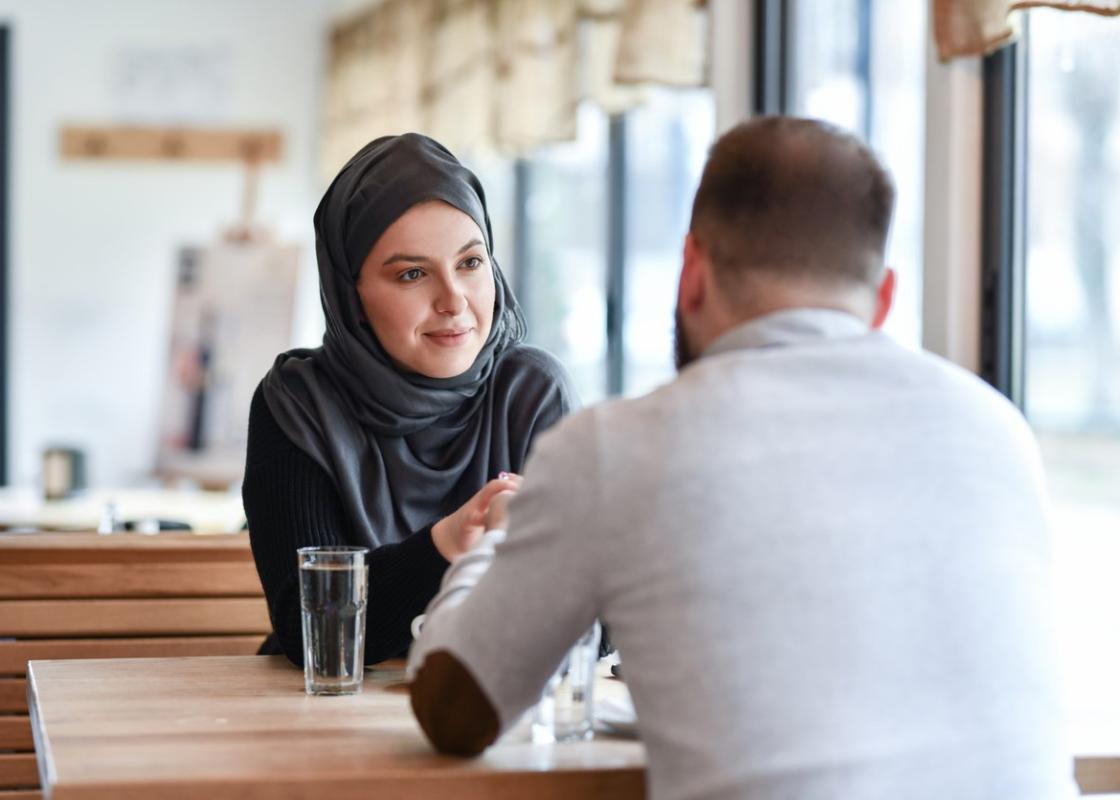 Kvinne med hijab og mann med ryggen til sitter på kafe