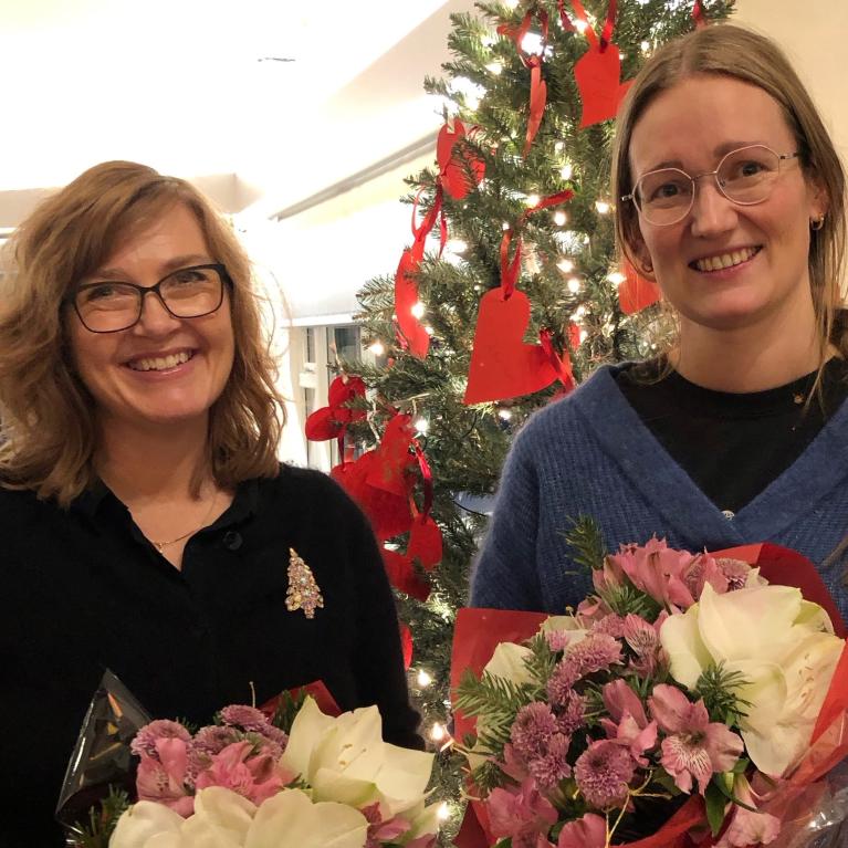 To kvinner med blomsterbuketter foran juletre